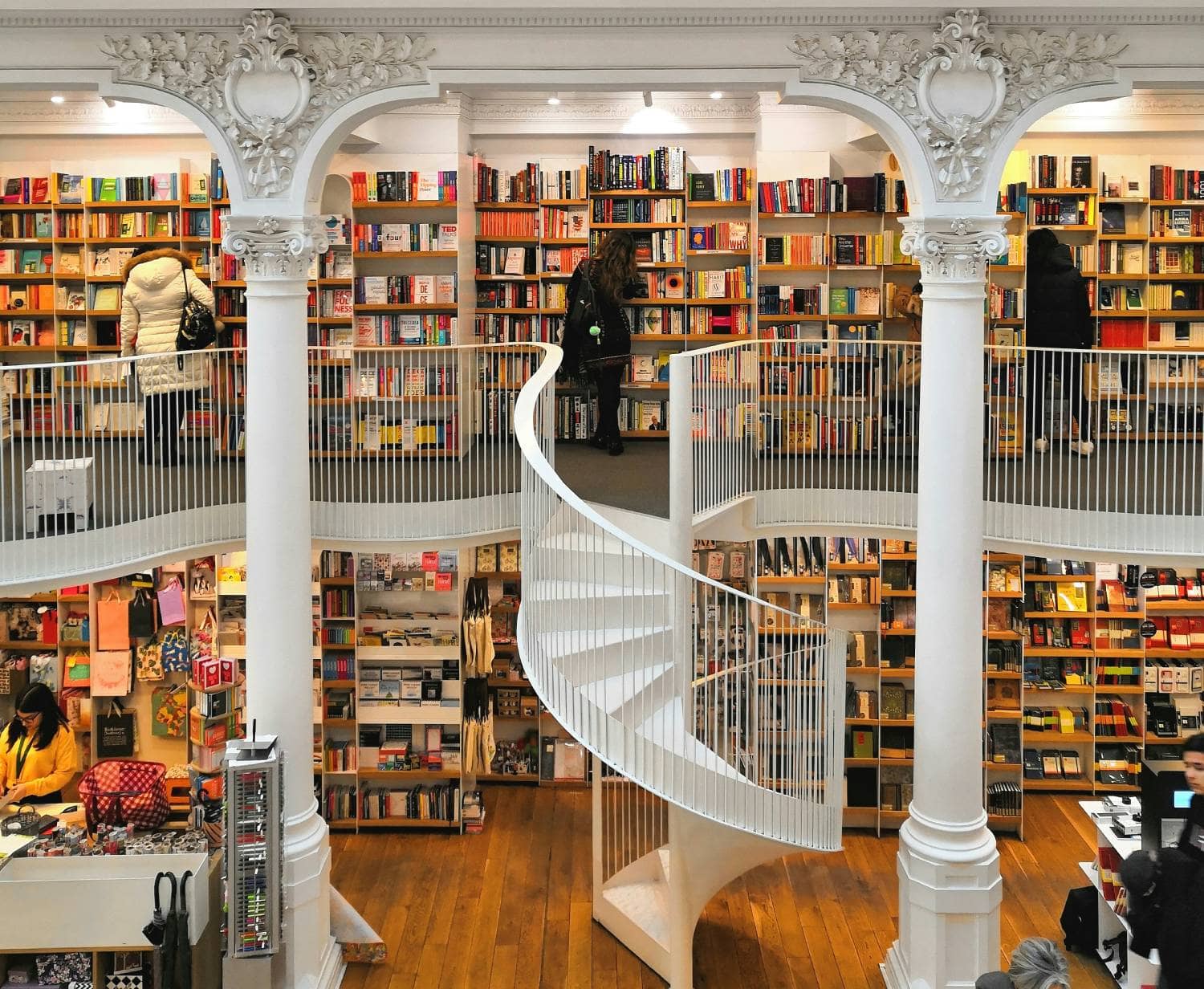 Readers browsing books in a bookshop with white columns and a spiral staircase